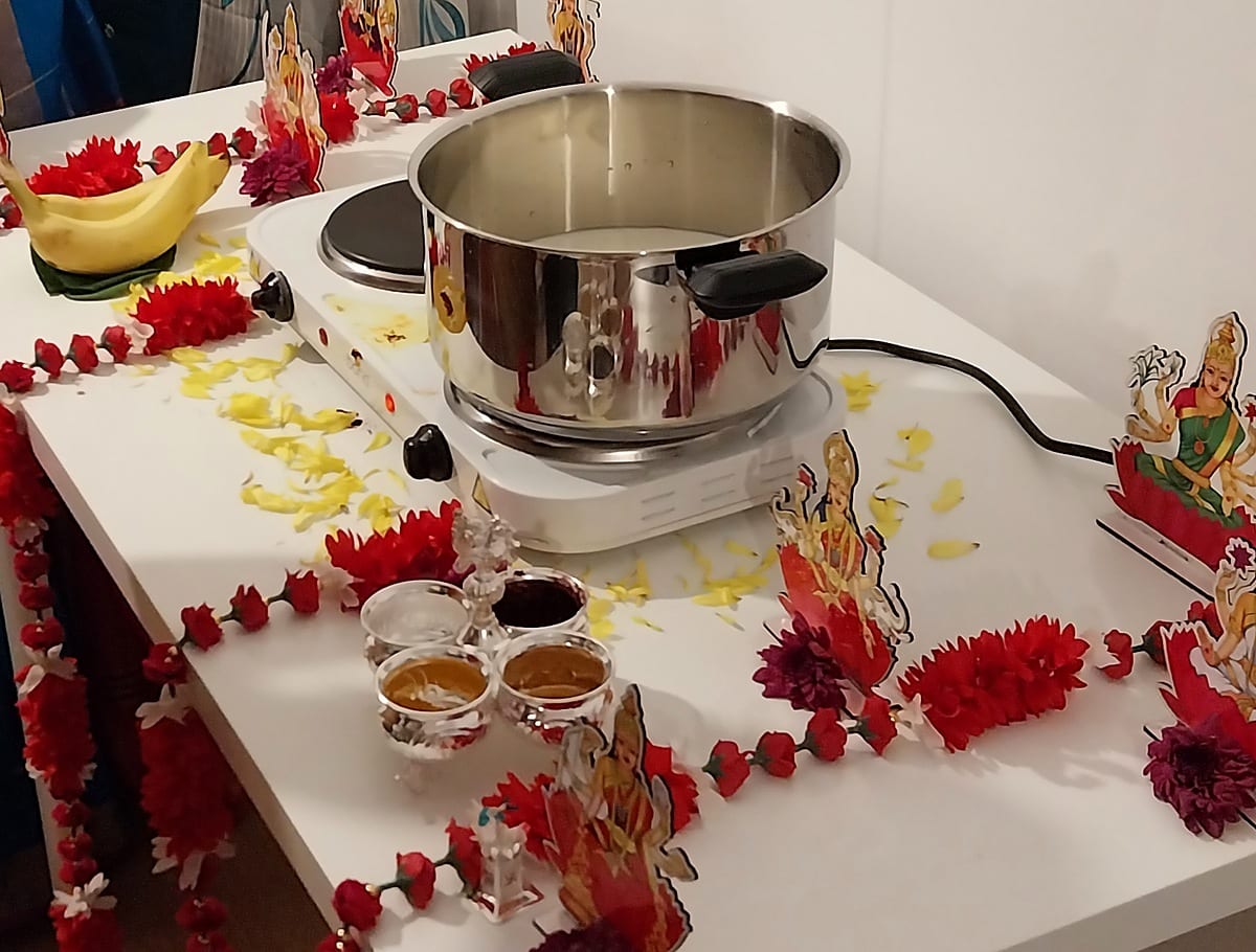The milk set to boil on the altar during a Griha Pravesh, with garlands, offerings, and the image of Lakshmi