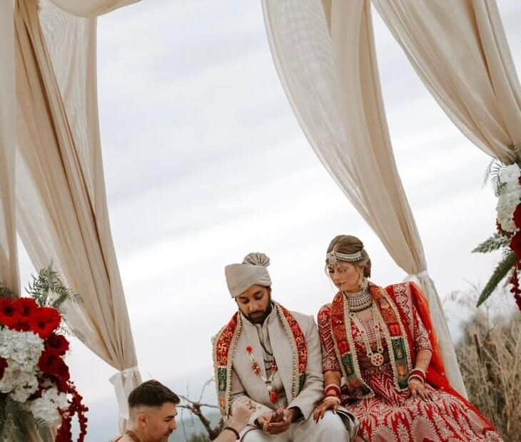 Pandit Sahadev conducting a Hindu wedding beneath the floral mandap on a hillside in Crete