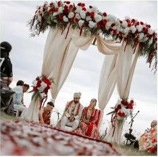A Hindu wedding beneath the floral mandap on a Greek hillside, the couple seated with the priest at the fire