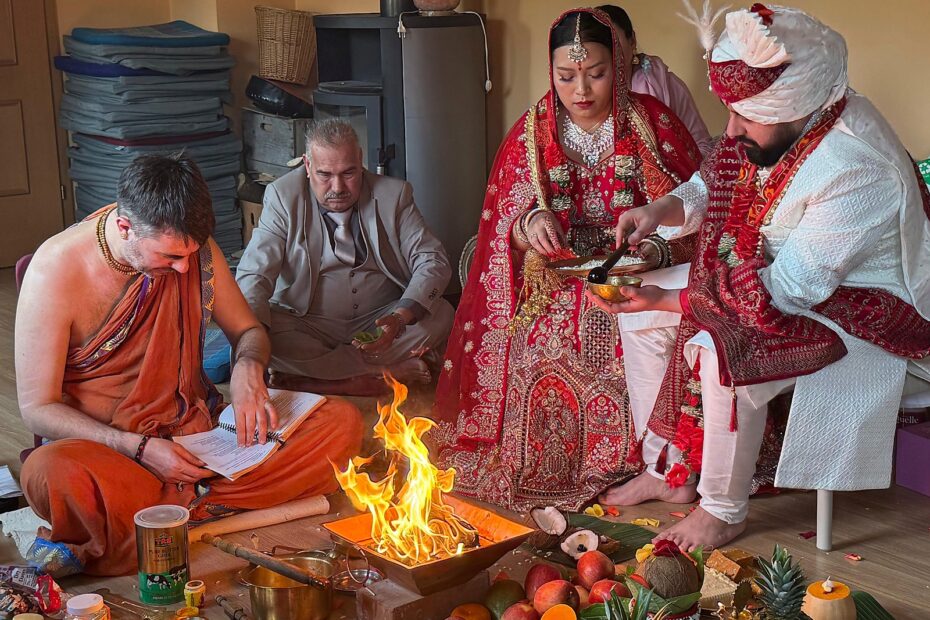 Bride and groom making the offering into the sacred fire during a Hindu wedding, the officiating priest reciting beside them