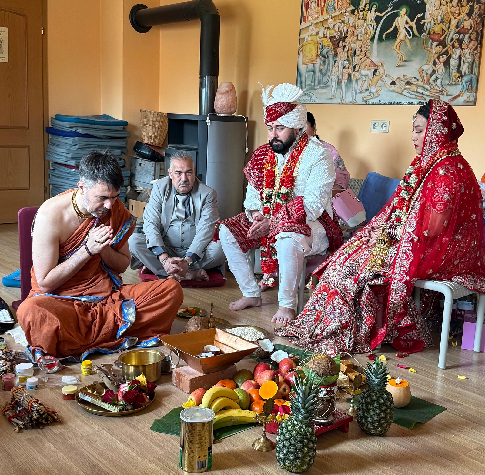 Pandit Sahadev in prayer while officiating a Hindu wedding, the couple seated before the offerings
