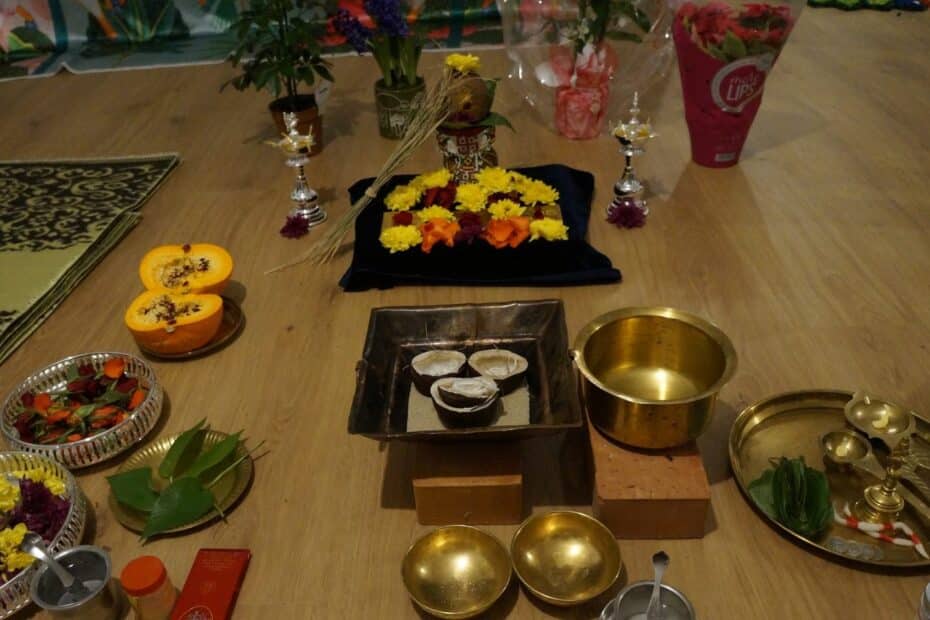 Copper homa kuṇḍa with coconut halves, brass vessels, offering ladles, flowers and silver lamps before a decorated kalaśa